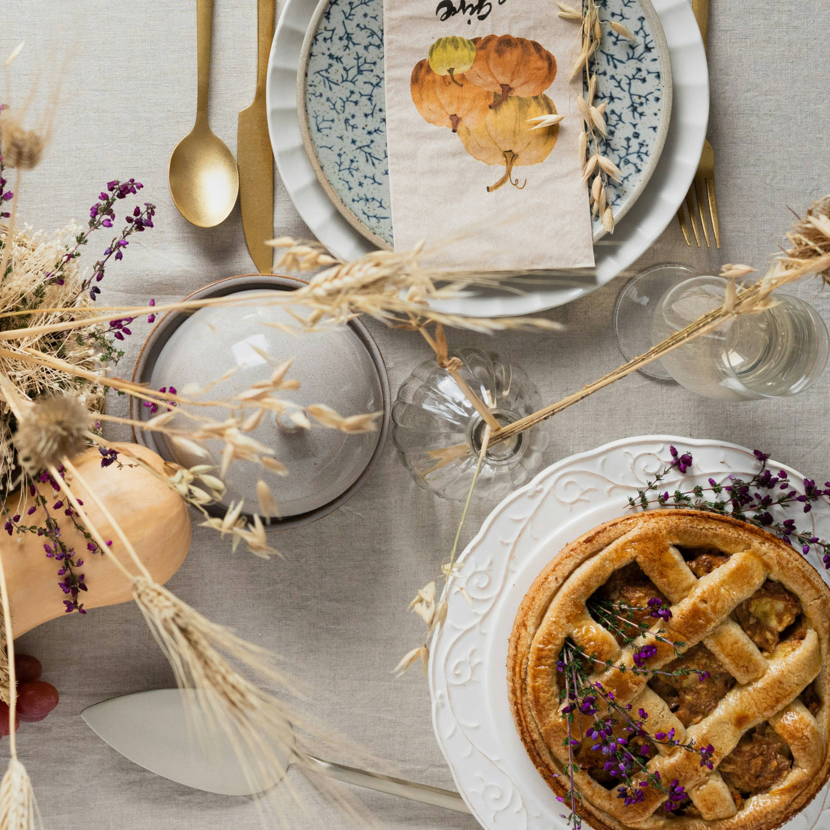 Dining table with place setting, fruit pie and dried flower arrangement