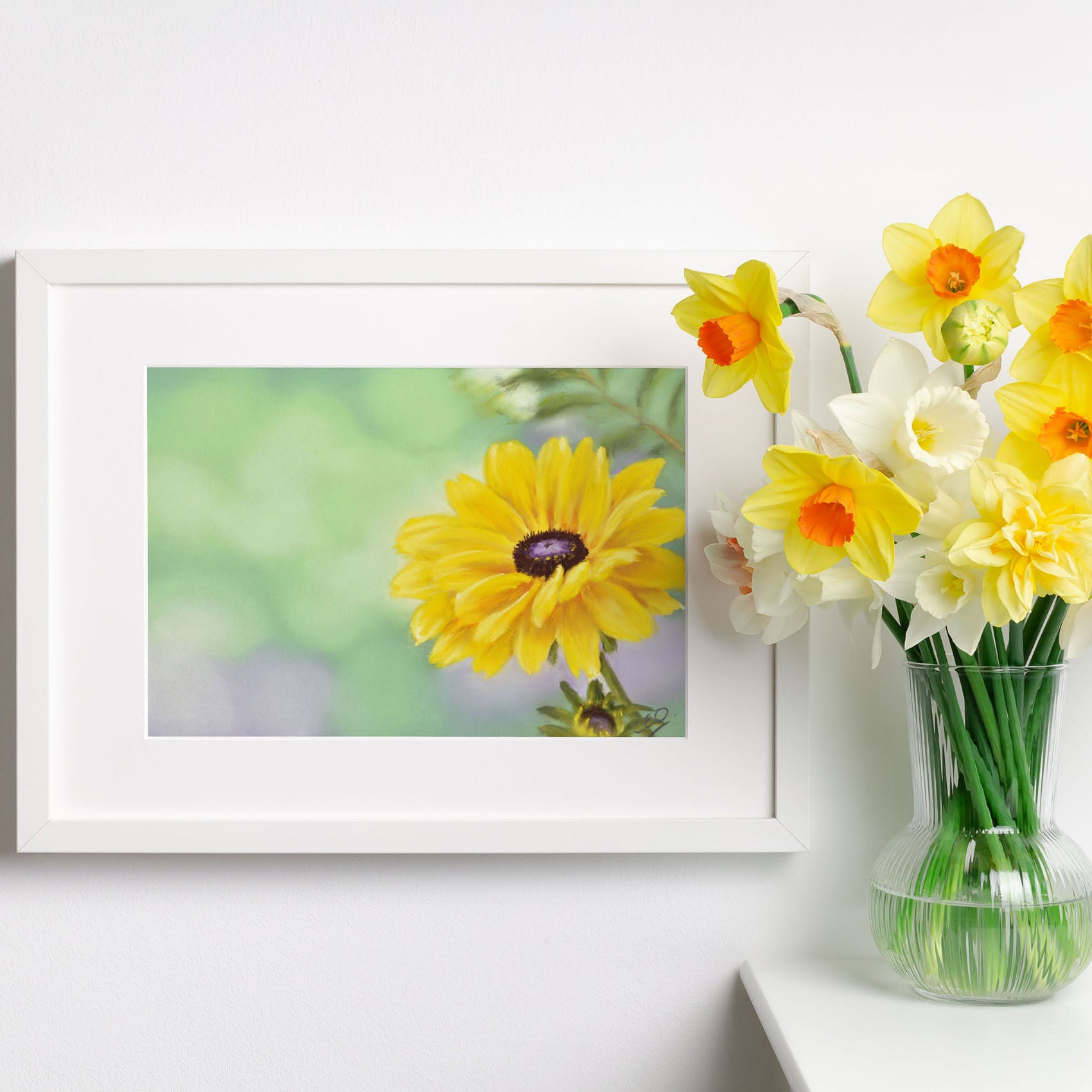 Yellow dahlia flower art print in white frame next to vase of daffodils