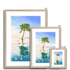 Palm tree set against blue sky and reflecting in clear turquoise water. Fine art print in a natural frame with a white mount. Different sizes, smallest at the front.