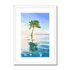 Palm tree set against blue sky and reflecting in clear turquoise water. Fine art print in a white frame with a white mount. Portrait format.