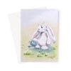 Adorable white rabbit watering the daisies with a little blue watering can, art greeting card. Portrait format